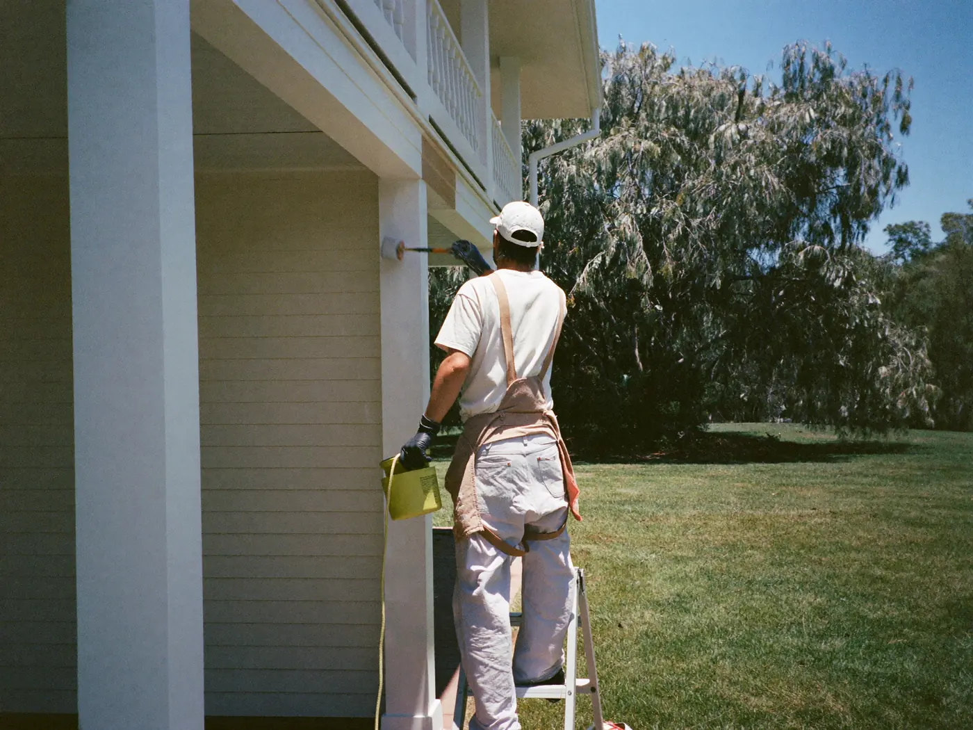 House painter on a ladder painting the weatherboards and verandah posts of a house white