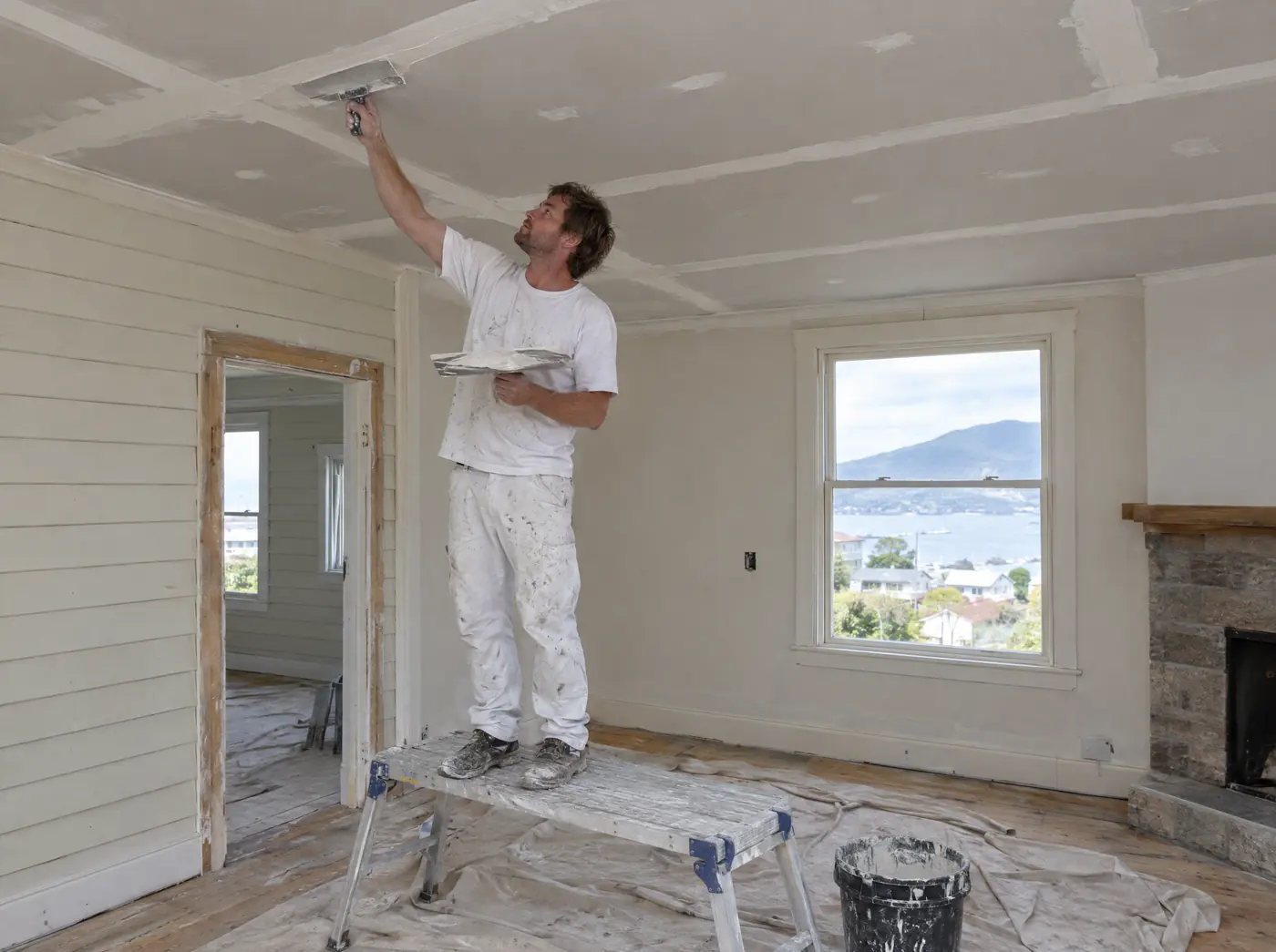 Plasterer on a trestle setting the joints of a new plasterboard ceiling in a weatherboard house