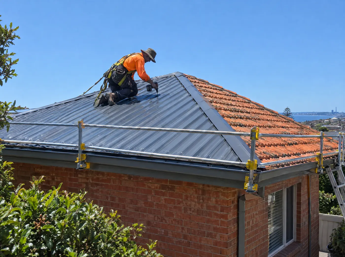 Roofer in a harness screwing down new steel roof sheets, the old terracotta tiles still on the other side of the roof
